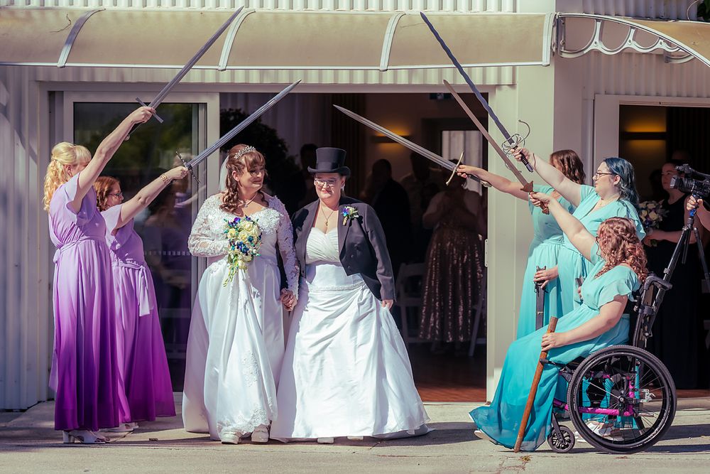 Wedding party members in turquoise and purple dresses pose together with brides in formal gowns for group photos.