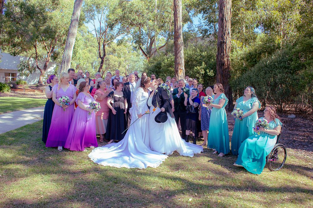 Wedding party in coordinated turquoise and purple dresses poses for outdoor photos in a scenic garden setting.