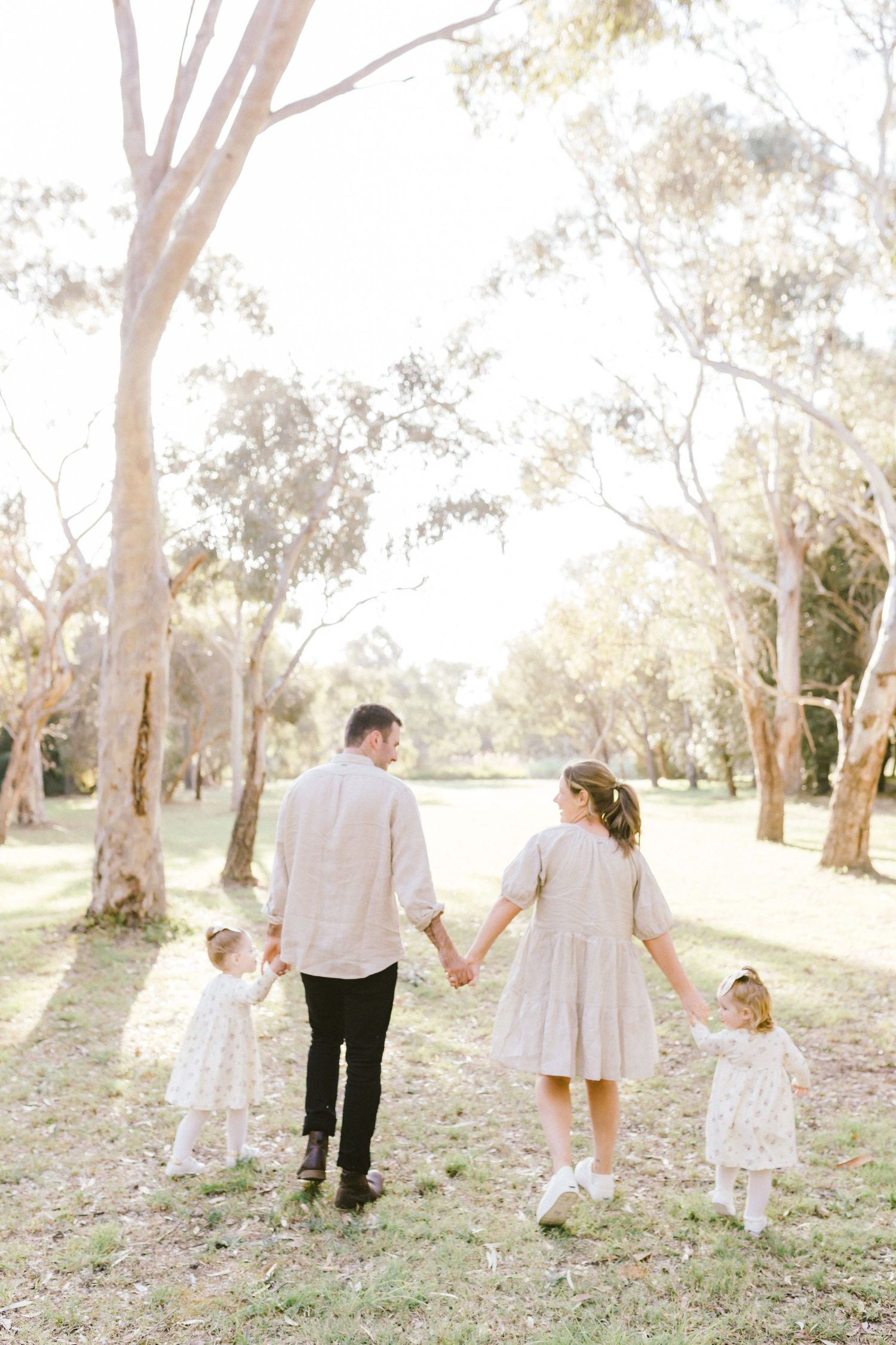 Family walking together through a sunlit eucalyptus grove in white and neutral outfits during a golden afternoon.