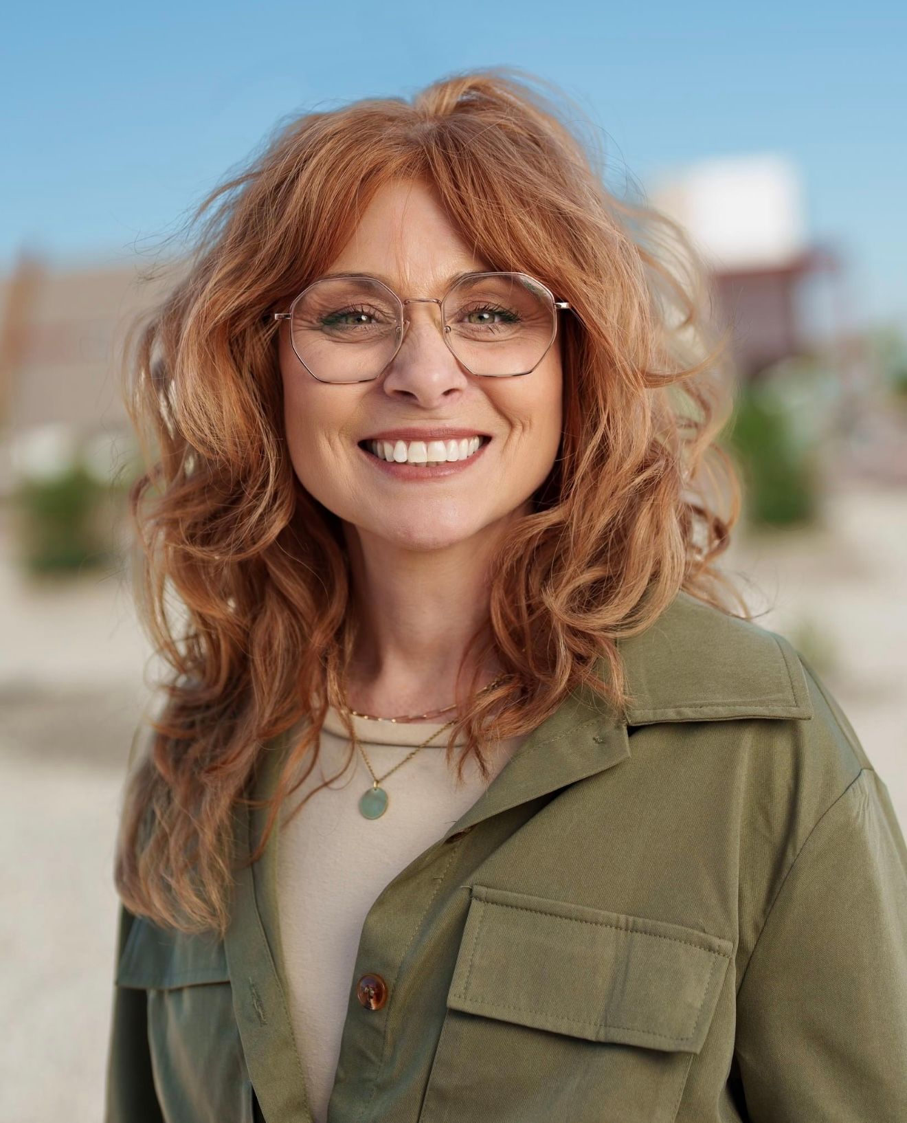 Portrait series of woman with wavy red hair wearing olive jacket against outdoor setting.