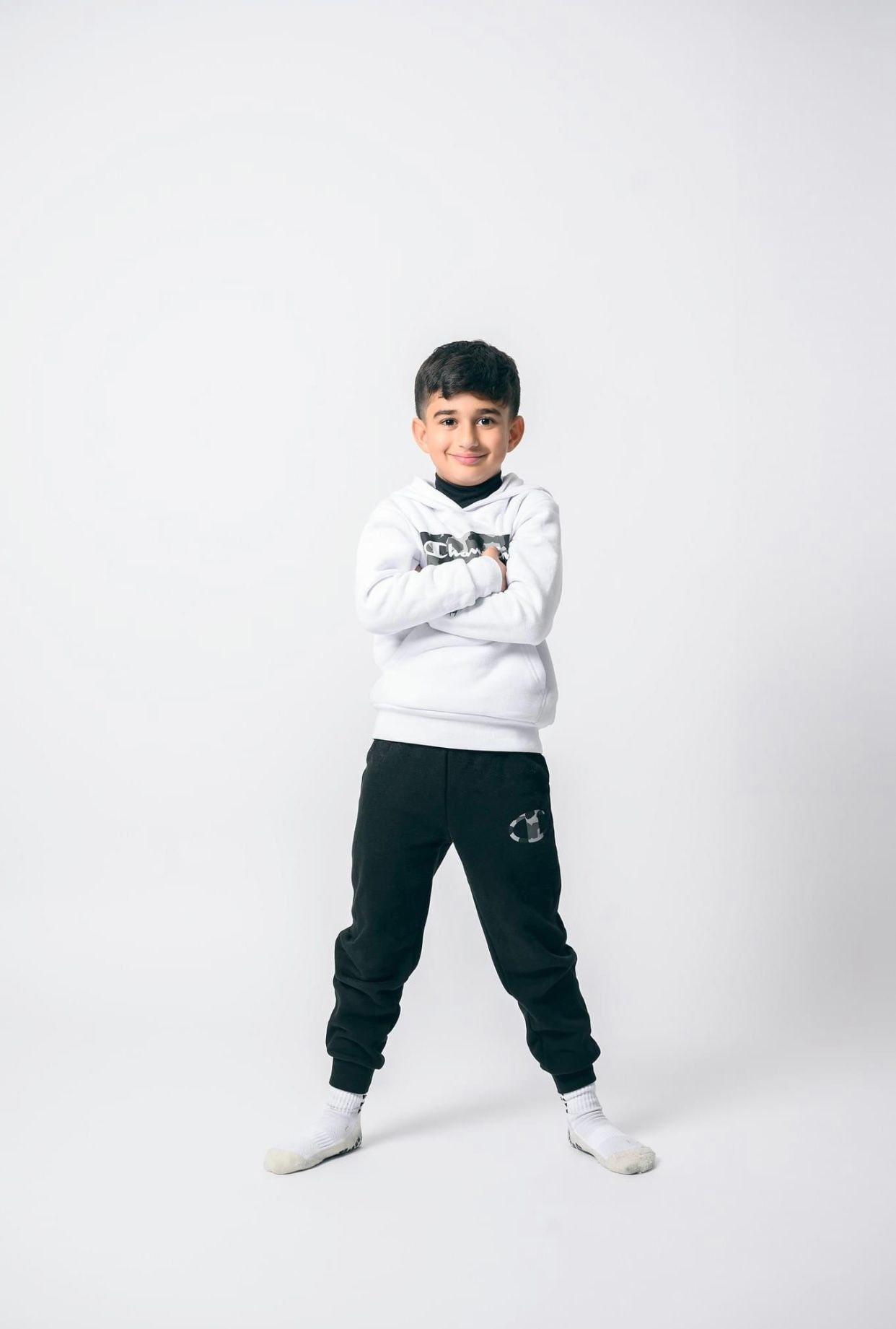 Young child in white and black outfit striking playful poses against white background.