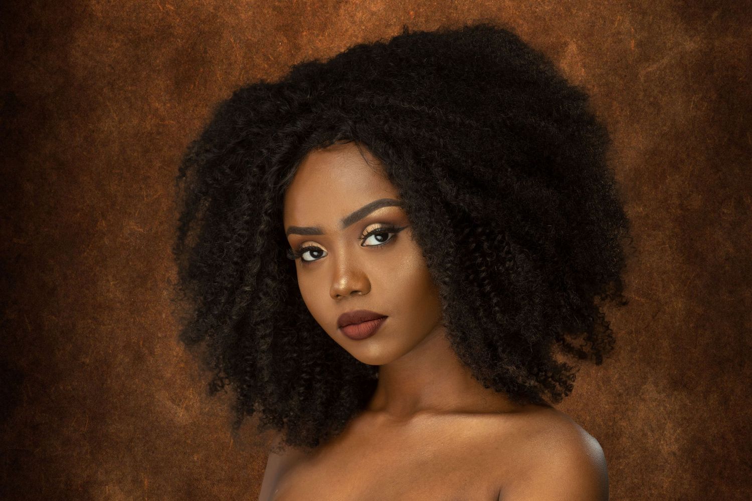Portrait series client with natural curly afro hair against brown backdrop.