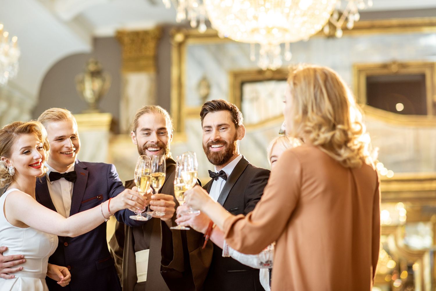 People at an elegant indoor event raise glasses in a champagne toast during a festive celebration with chandeliers.