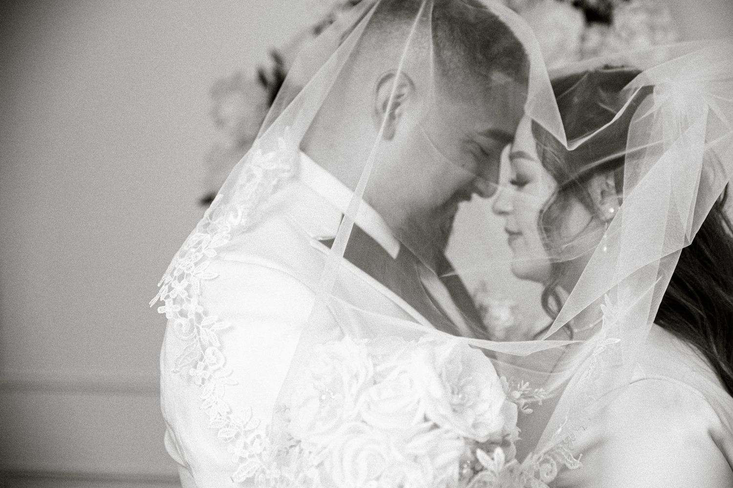 An intimate black and white portrait of newlyweds sharing a tender moment under a veil.