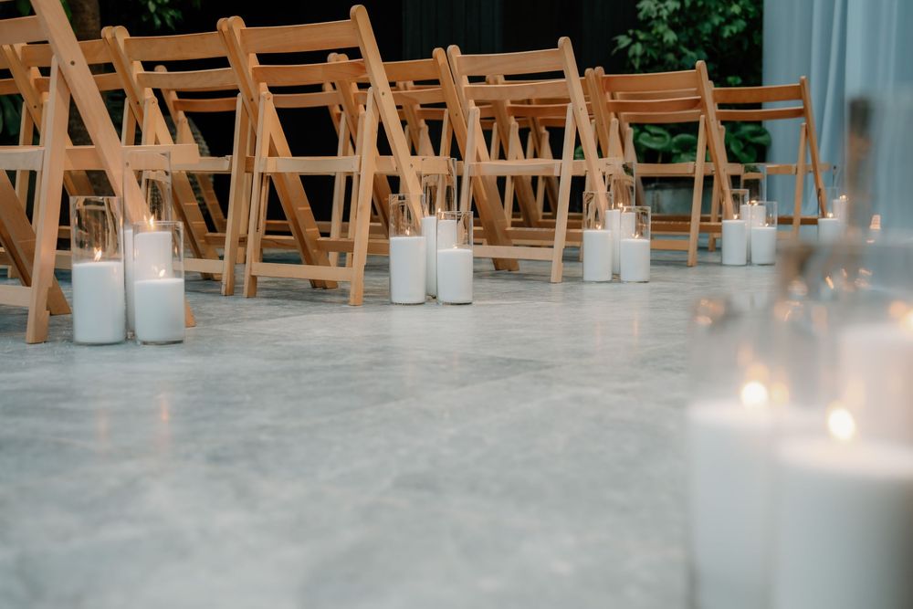 Wedding ceremony setup with rustic wooden folding chairs and glowing candle lanterns on a light gray floor.