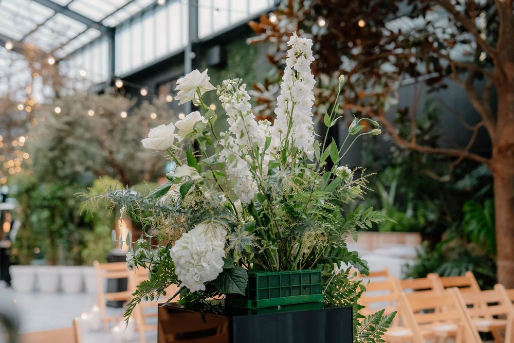 White floral arrangement in a green vessel with delicate wildflowers and greenery.