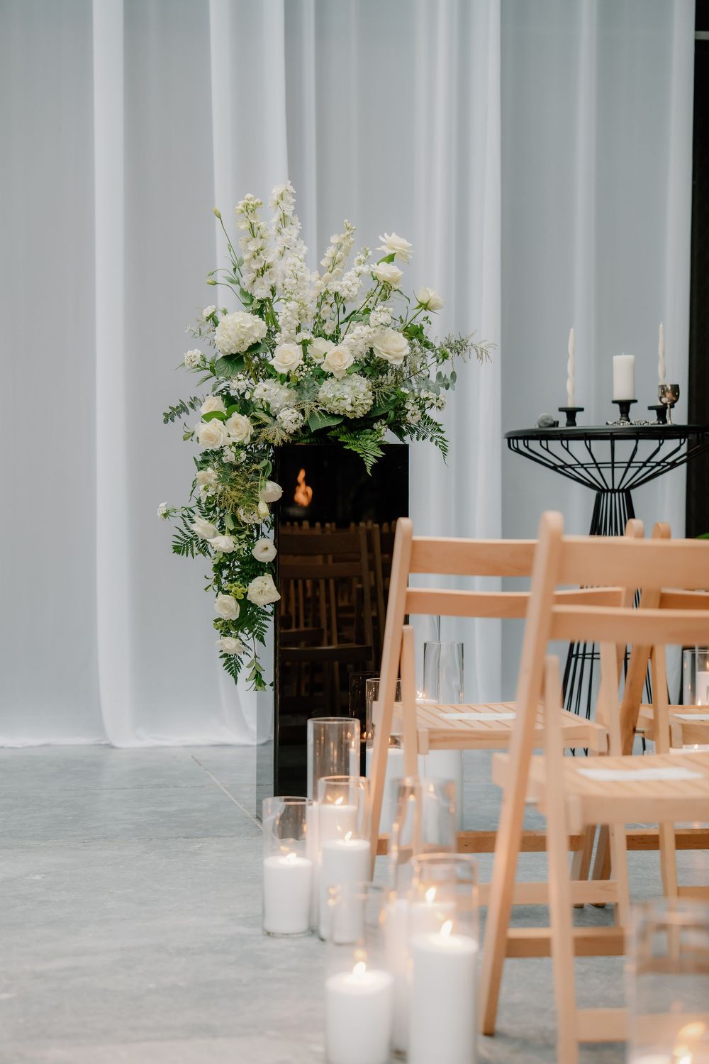 An elegant indoor wedding ceremony setup with wooden chairs and white floral arrangements along the aisle.