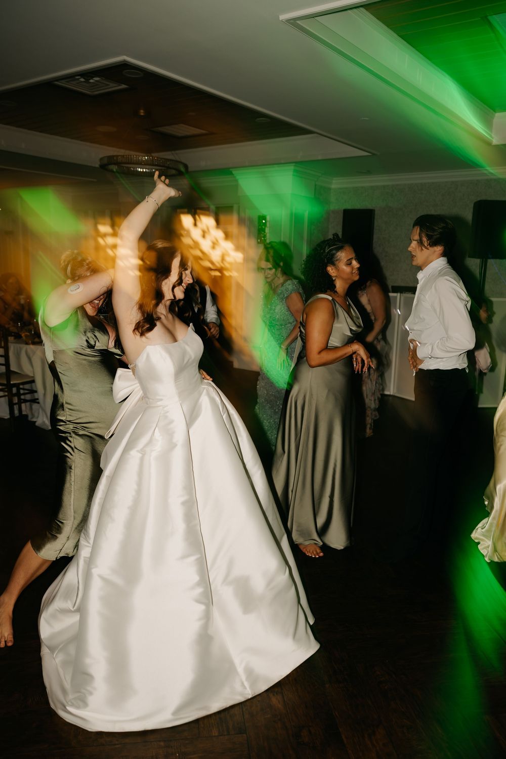 Wedding reception dance floor with green lighting and guests dancing in formal attire.