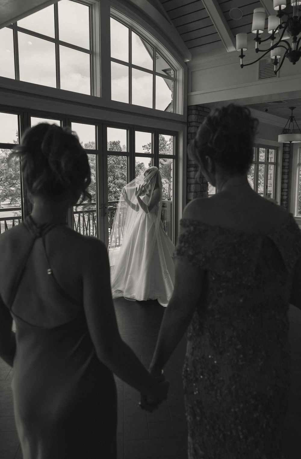 Wedding party silhouettes stand against bright windows in an elegant indoor venue.