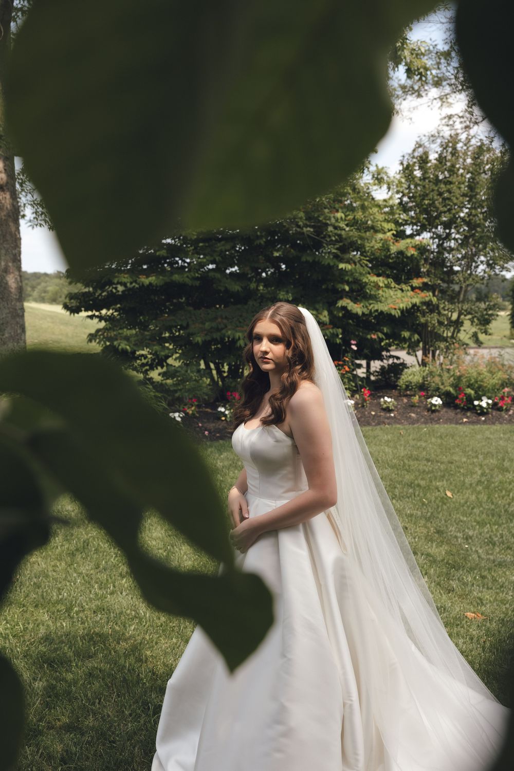 Bride in flowing white dress twirls outdoors in a garden setting.