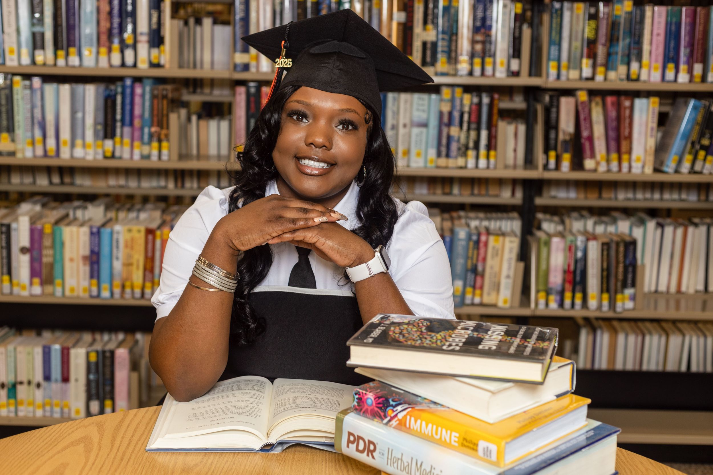 Academic portrait session in a library with graduation cap and books.