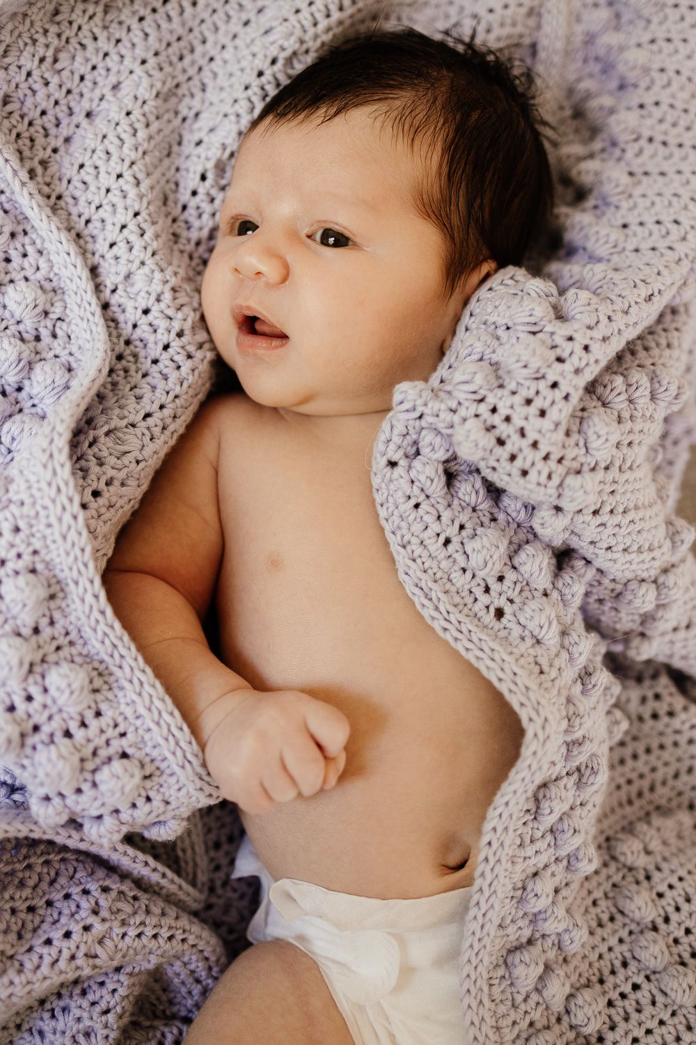 Newborn baby is wrapped in a knitted blanket for his in-home newborn session in Saratoga