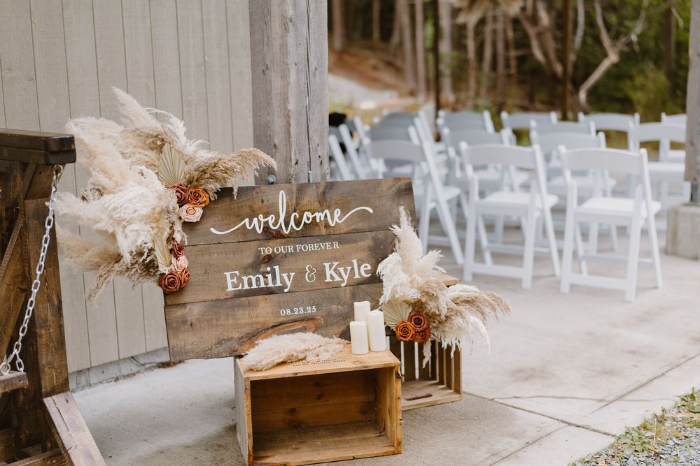 Rustic wedding setup with white chairs, wooden decor and floral arrangements arranged outdoors for a ceremony.