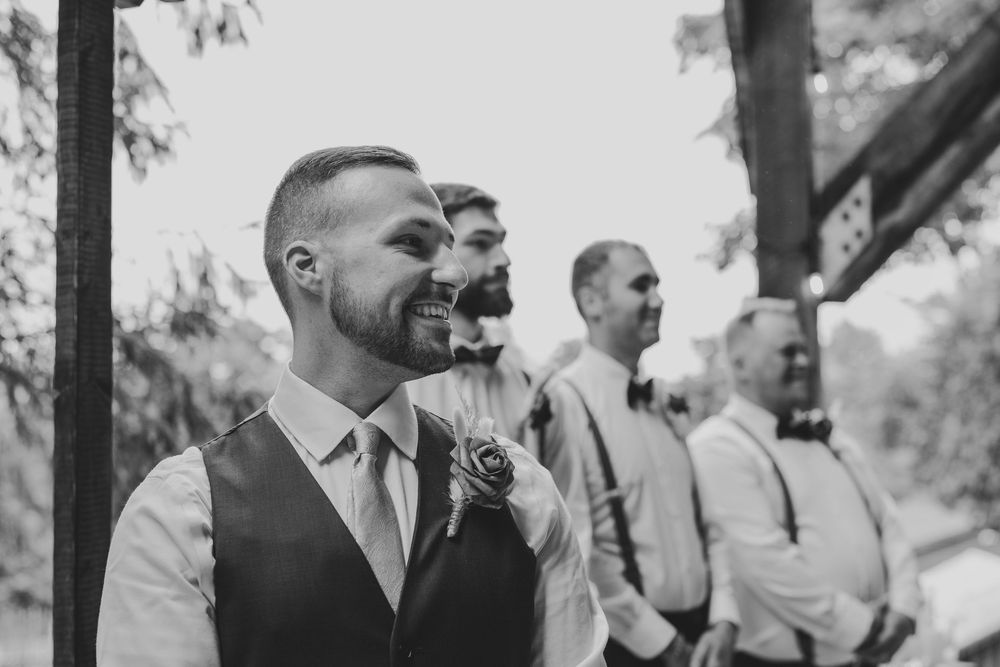 Joyful guests laugh and react during an emotional outdoor wedding ceremony among trees and natural surroundings.