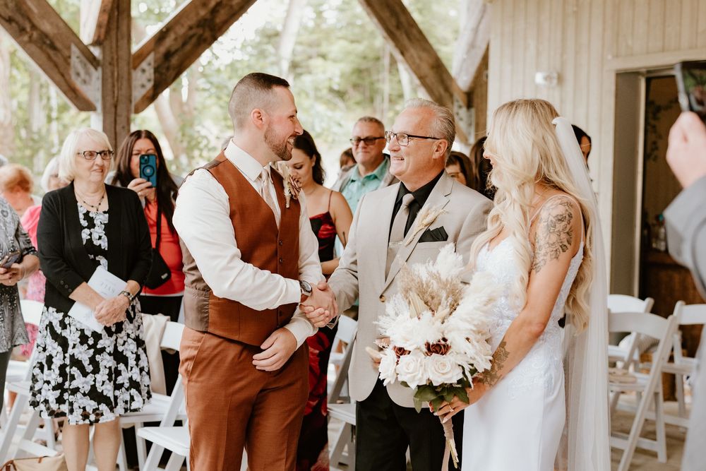 Emotional wedding ceremony moment captured under a rustic wooden pavilion with guests looking on.