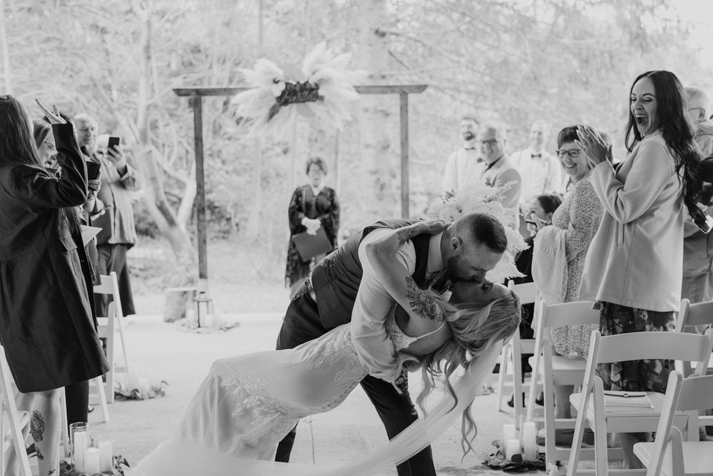 Black and white photo captures dramatic dip kiss during outdoor wedding ceremony.