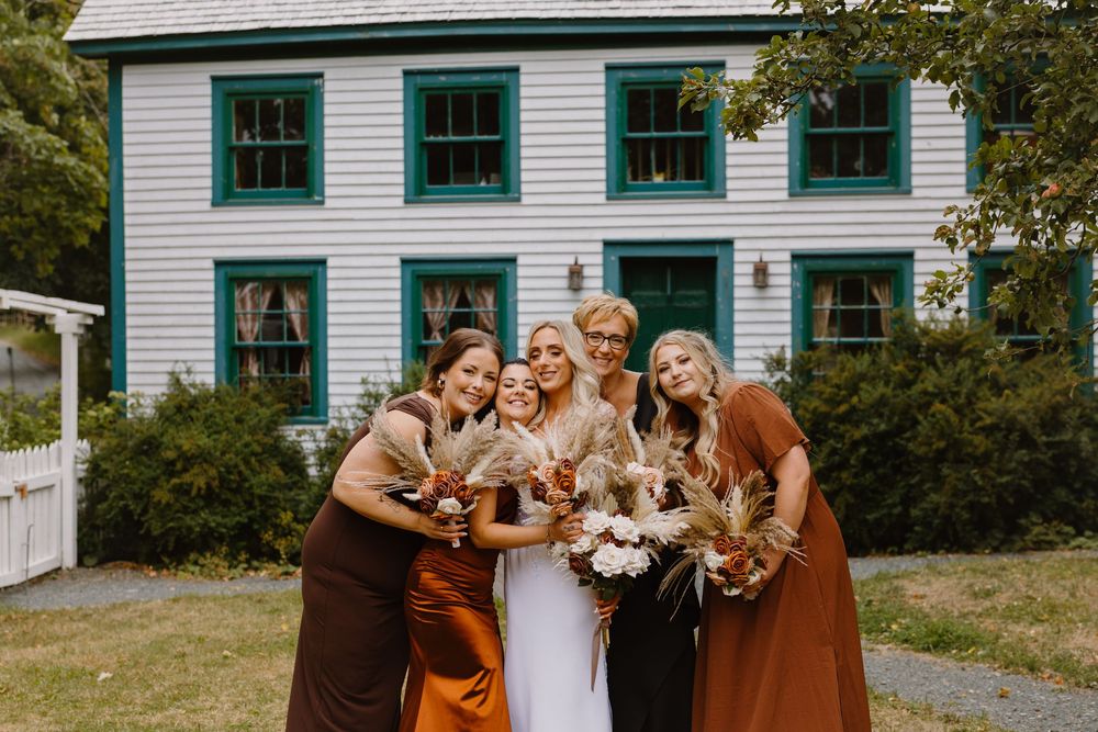 Wedding party gathered outside a white historic building with green windows, laughing and embracing.