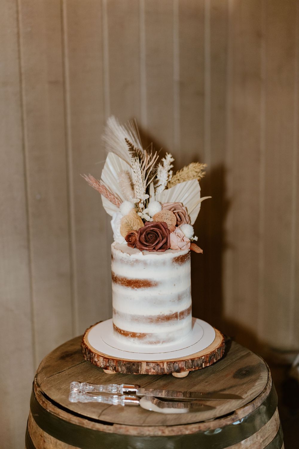 Semi-naked white wedding cake decorated with dried flowers and roses on a wooden cake stand.