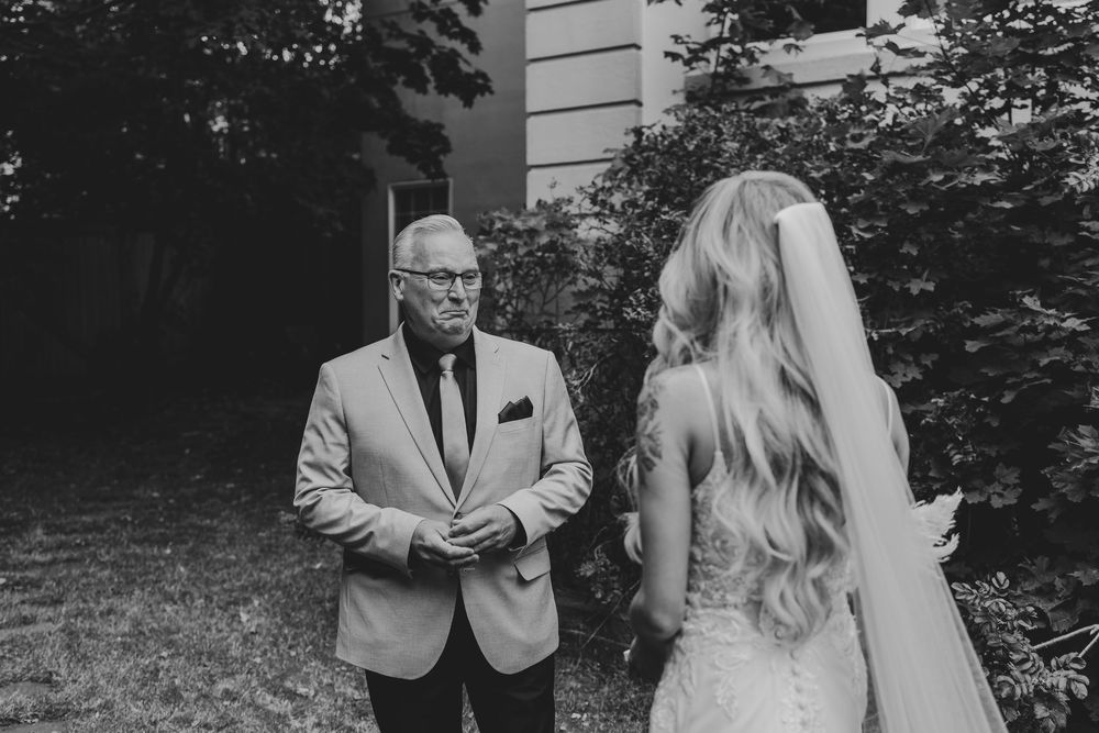 Tender moment between a bride in white dress and gentleman in gray suit before ceremony.