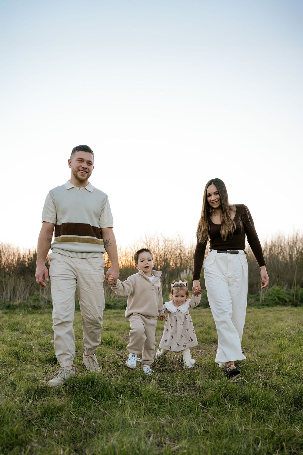 A group of people wearing coordinated white and beige outfits walk together through a grassy field at sunset.