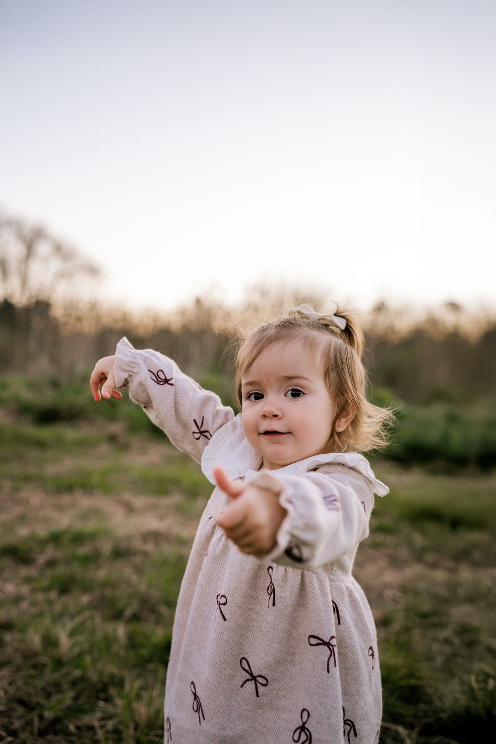 Child wearing a beige sweater runs and plays outdoors at sunset in a grassy field.
