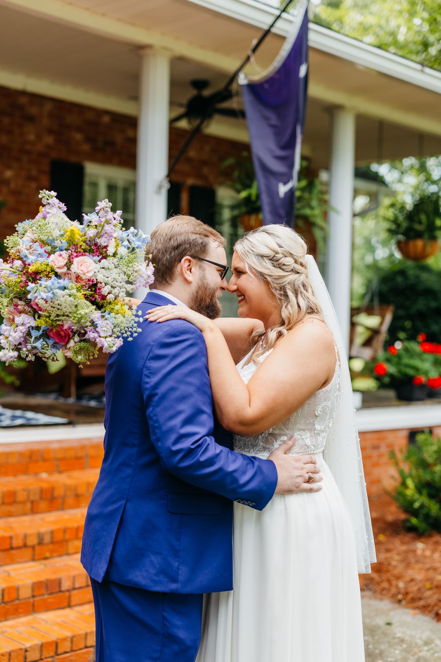 Wedding couple sharing romantic kisses in front of a porch with colorful flowers.