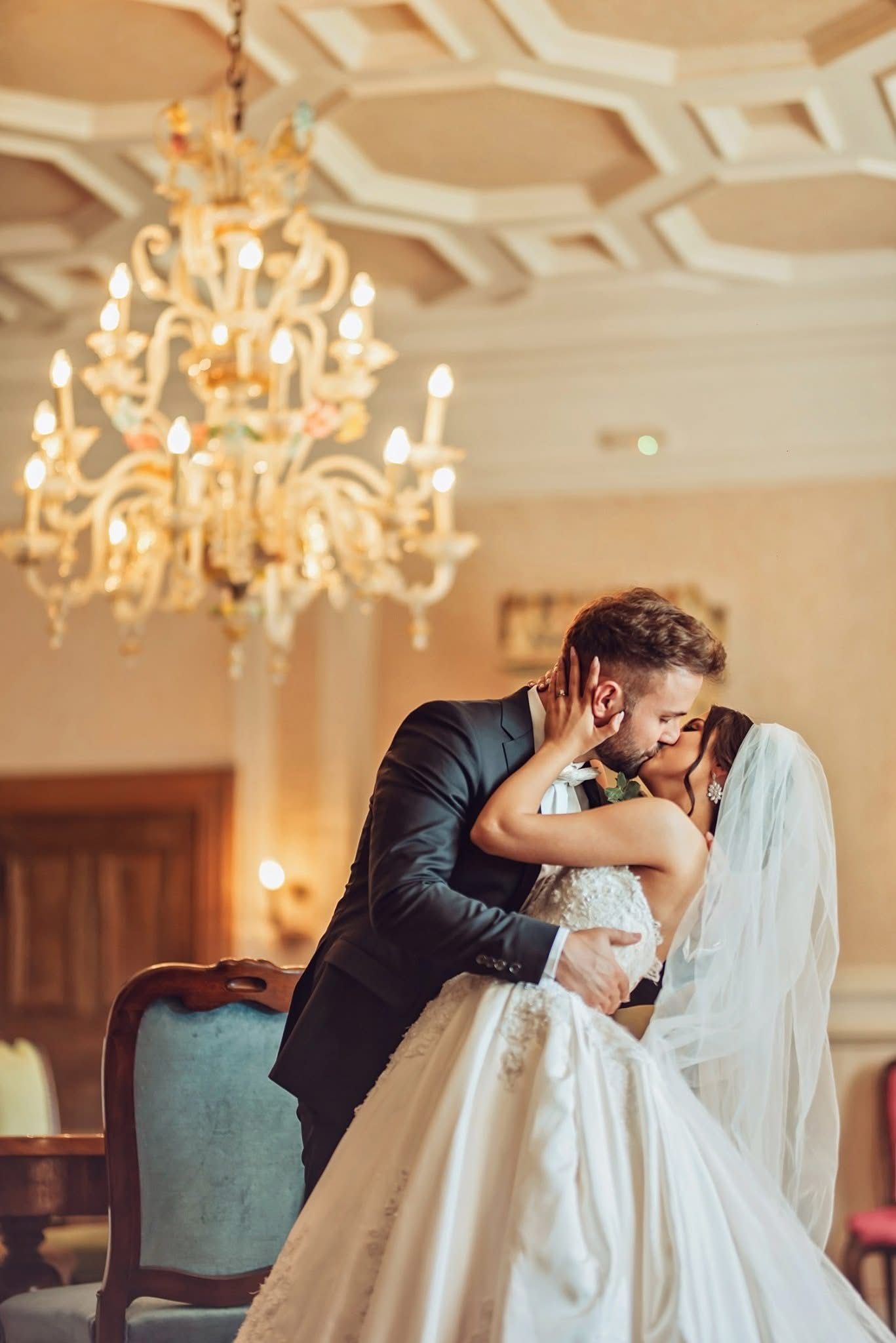 A romantic moment between newlyweds in an elegant ballroom with ornate chandeliers and soft lighting.