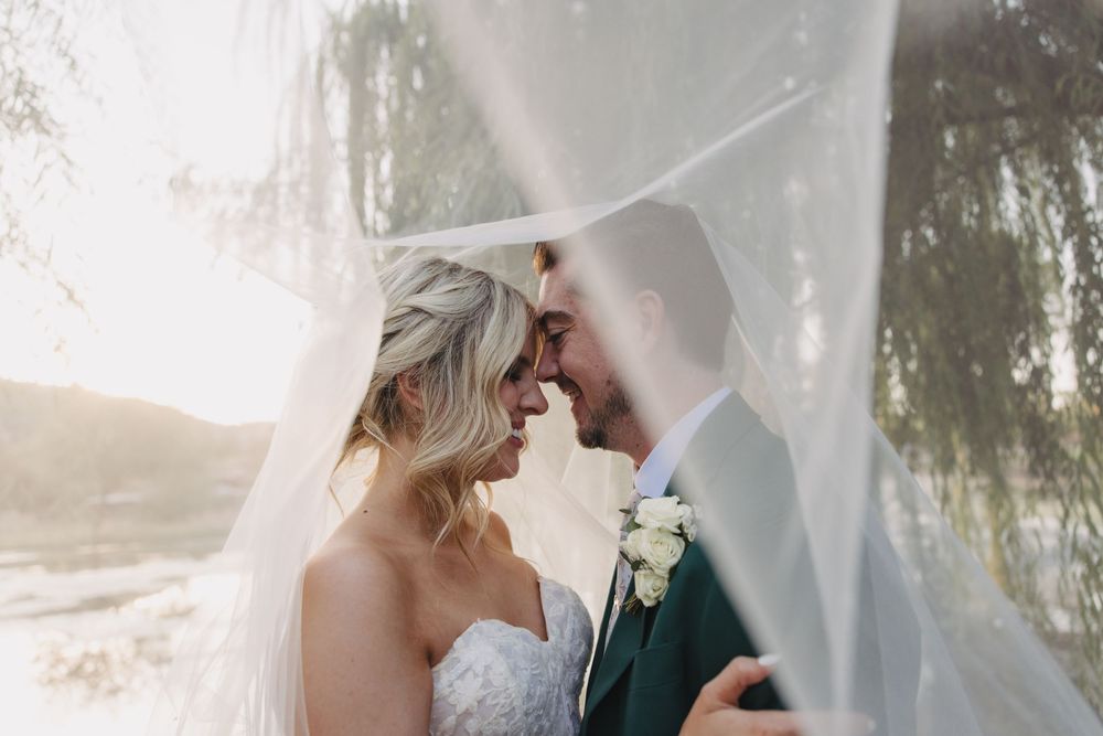 Romantic wedding couple embraces under a cozy white umbrella in the rain.