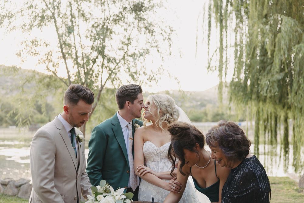 Wedding guests gather for photos under a willow tree at sunset.