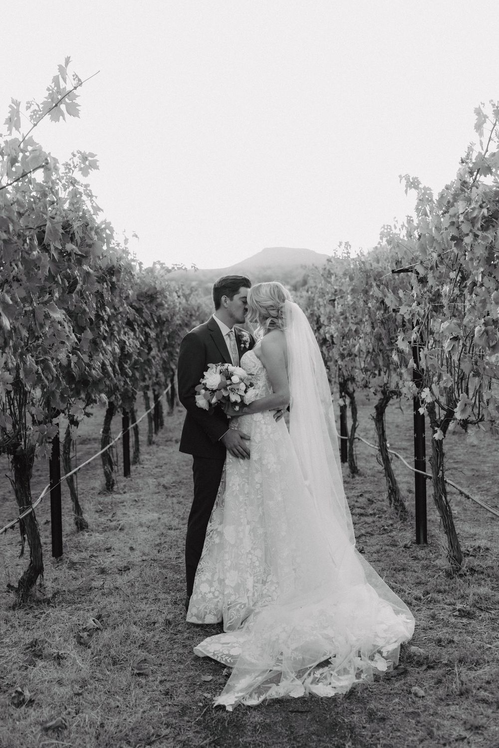 A romantic moment captured in black and white between newlyweds in a hillside vineyard.