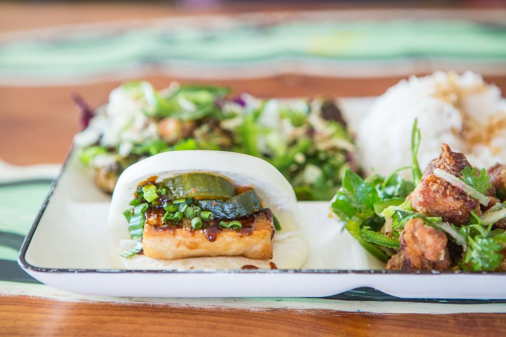 Asian fusion bao buns filled with meat and fresh herbs served with a side salad on a white rectangular plate.