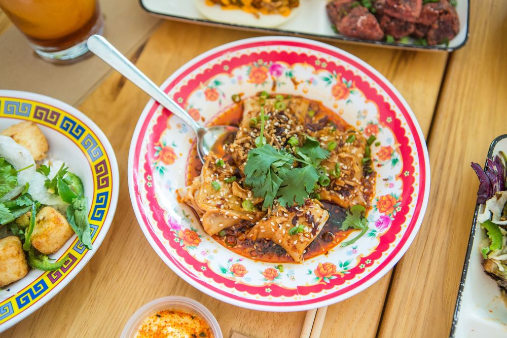 Stir-fried rice noodles topped with fresh cilantro served on decorative plate with Chinese-style dishes on wooden table.