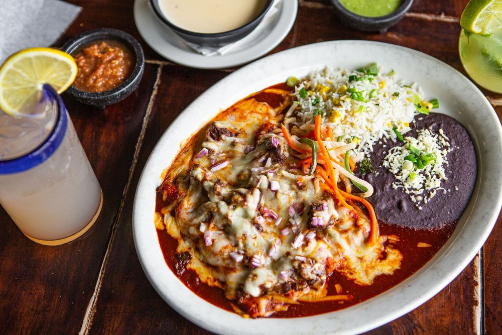 Colorful assortment of Mexican dishes including enchiladas and tacos served on white plates with garnishes and sauces.