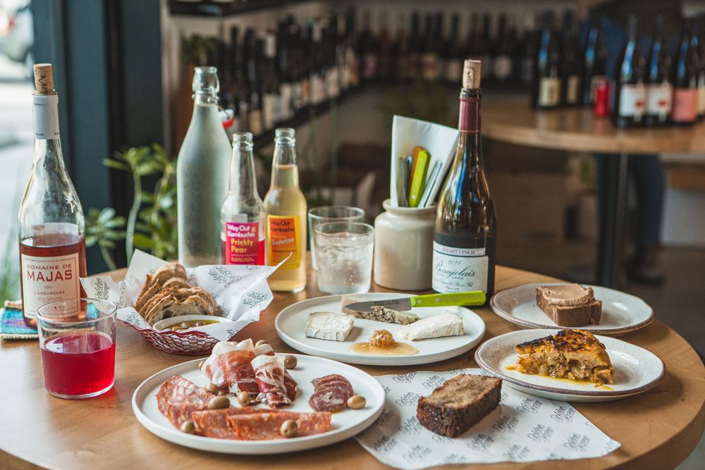 Restaurant table spread with multiple plates of food and drinks, including cocktails, wine bottles, and various dishes.