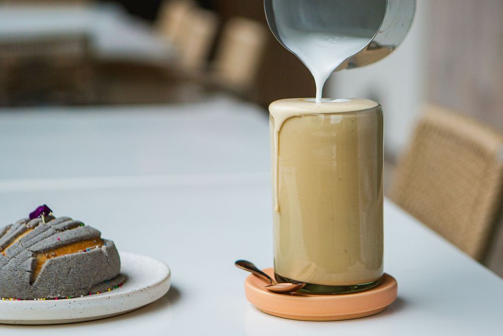 Hand pouring tea or coffee into ceramic beige mugs on white table with soft natural lighting.
