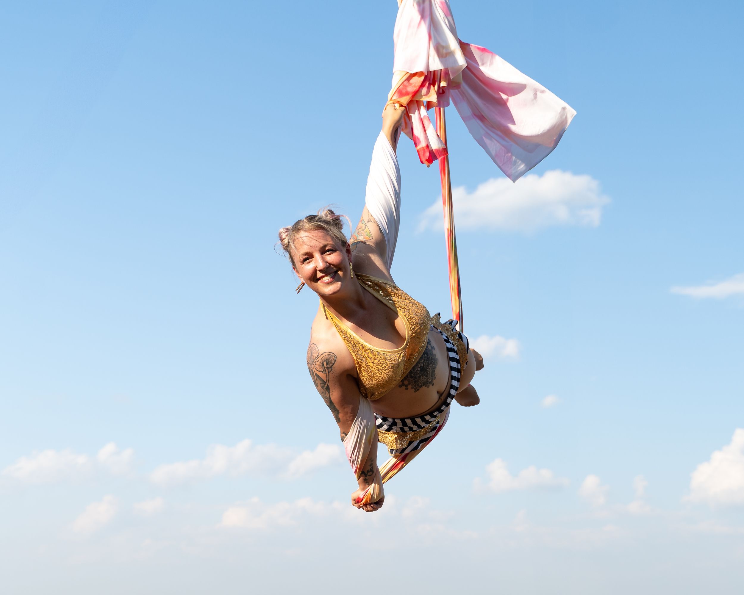 A person soars through the blue sky while holding onto a pink flag pole in a dramatic airborne moment.