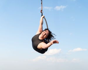 An aerial acrobat performs a graceful sequence of poses while suspended from silk fabric against a bright blue sky.