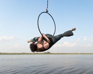 A person performs a dramatic floating dance pose while suspended horizontally over a beach with waves in the background.