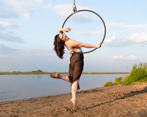 An acrobatic performer gracefully poses on a lyra hoop against a serene waterfront backdrop at sunset.