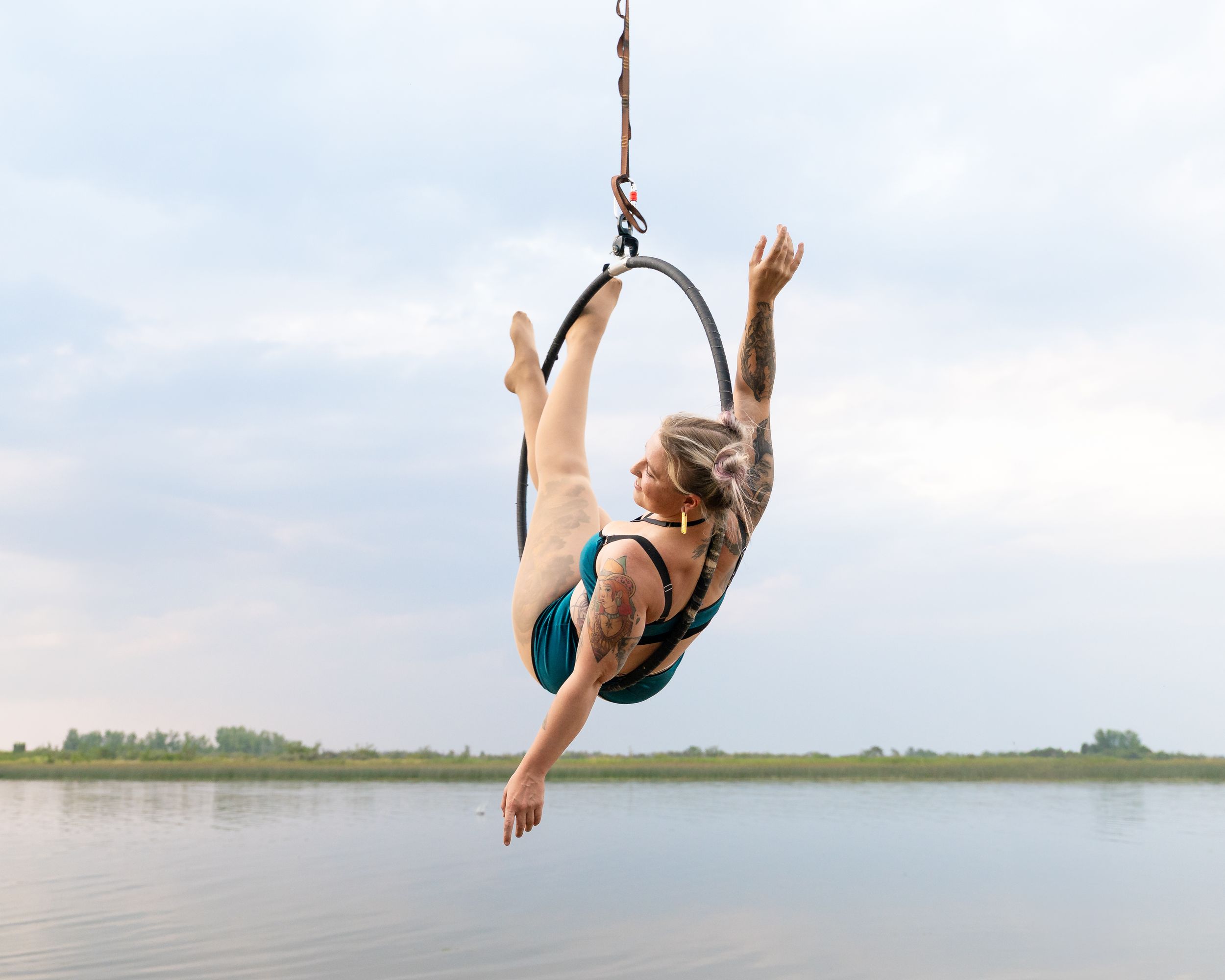 Acrobatic performer executes dynamic move on aerial hoop over serene lake waters.