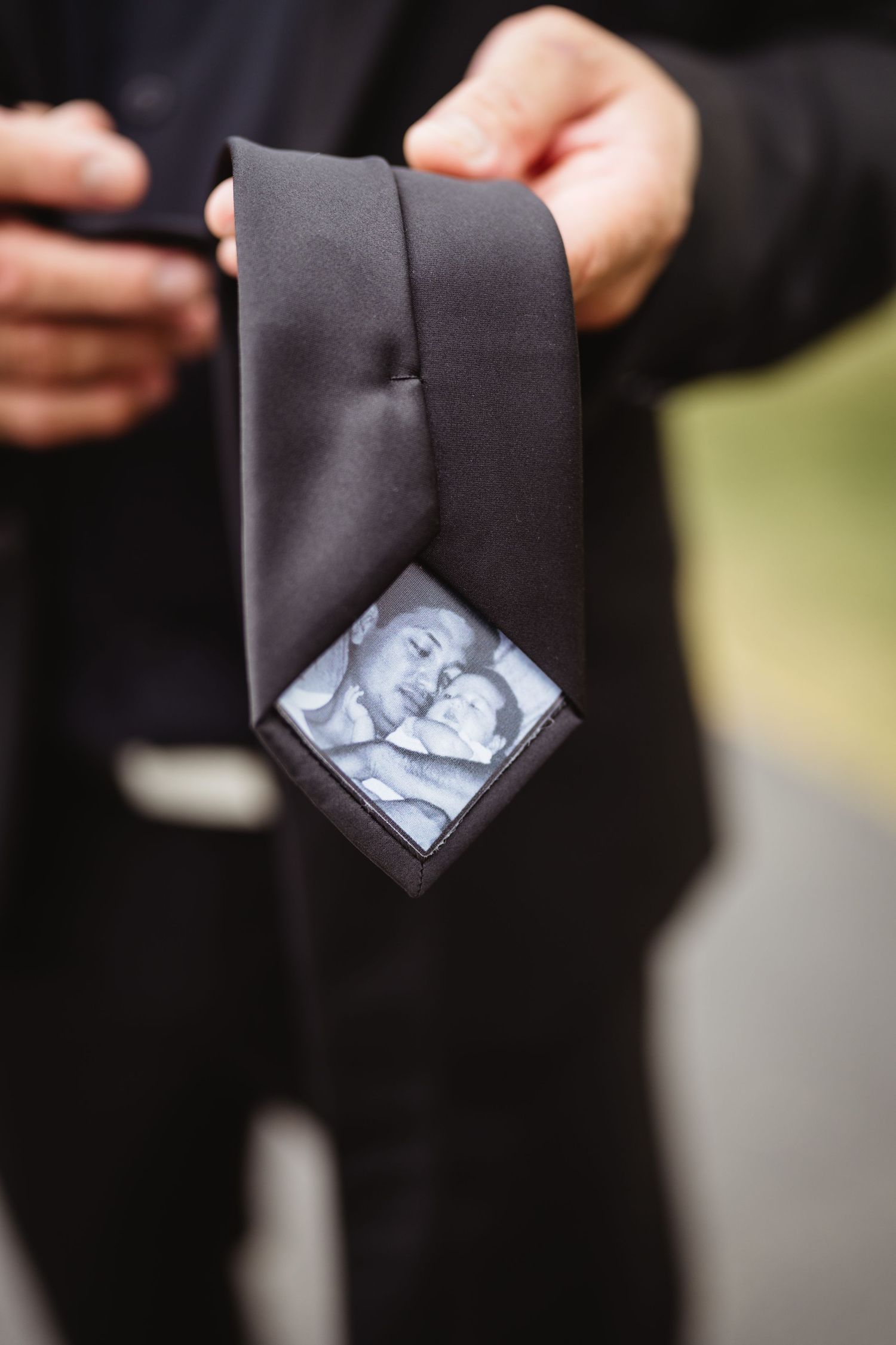 Close-up of a black tie with a sentimental photo tucked into its inner lining at what appears to be a formal event.
