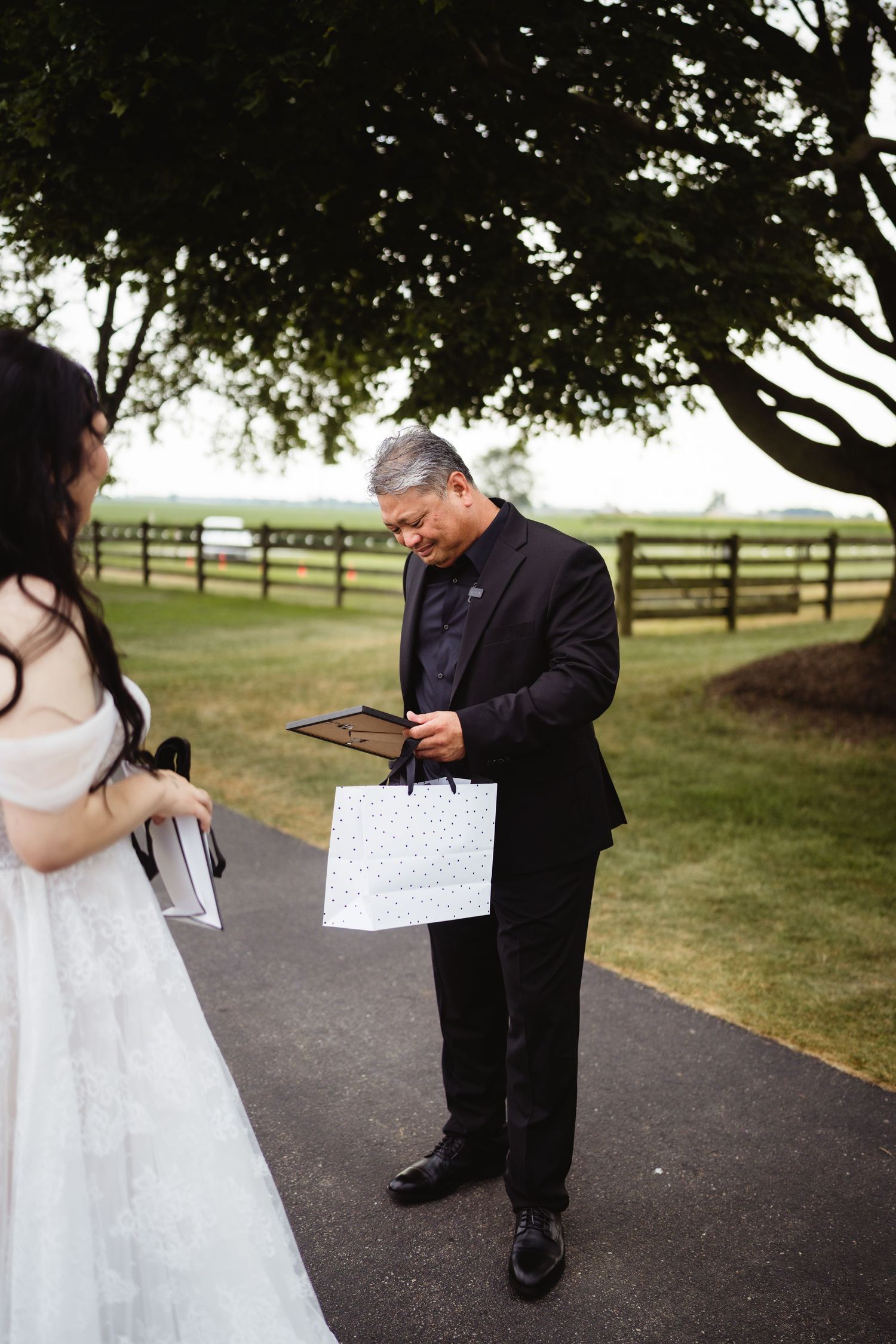 A couple shares a sweet first-look moment reading handwritten notes to each other on a tree-lined path.