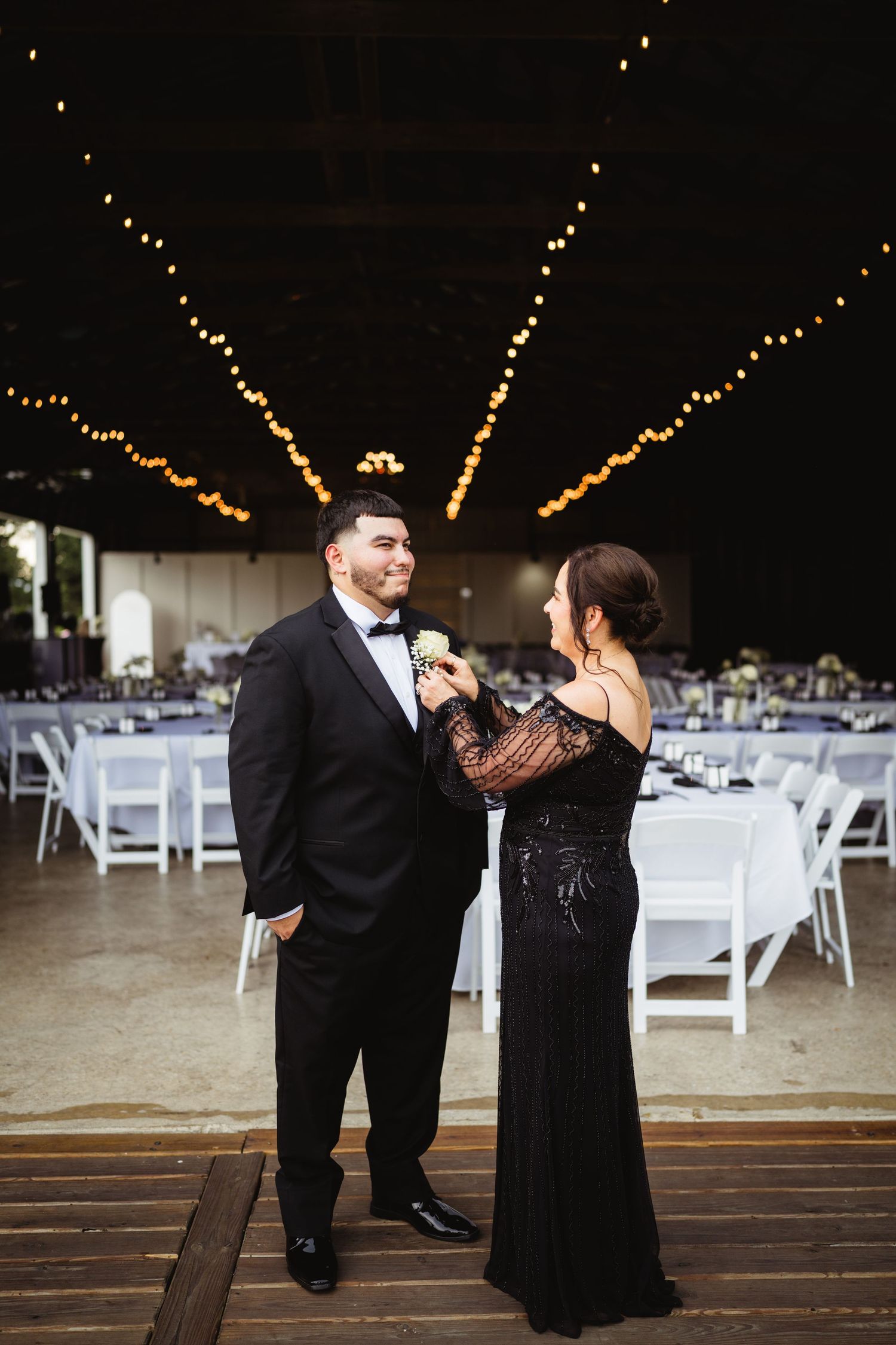 A formal event setting with string lights overhead and white reception tables arranged in an elegant indoor venue.
