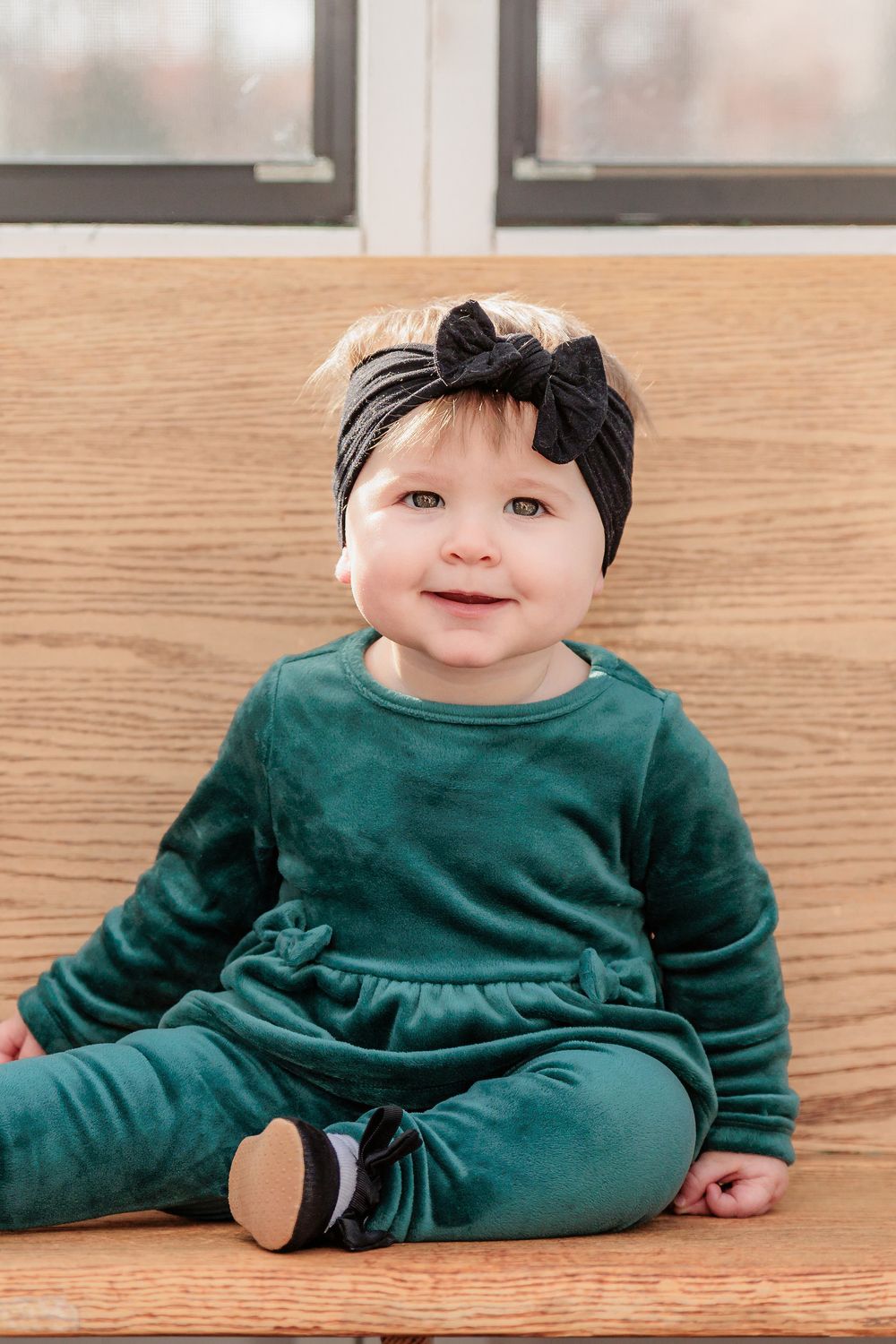 Adorable baby in dark green velvet romper sitting on wooden floor in indoor photo series at Turkey Trac Farm in Millville NJ
