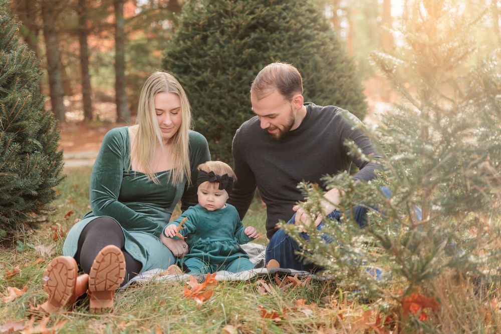 A family sits on grass filled with colorful fall leaves during an outdoor autumn photo session in warm sunlight at Turkey Trac Farm in Millv