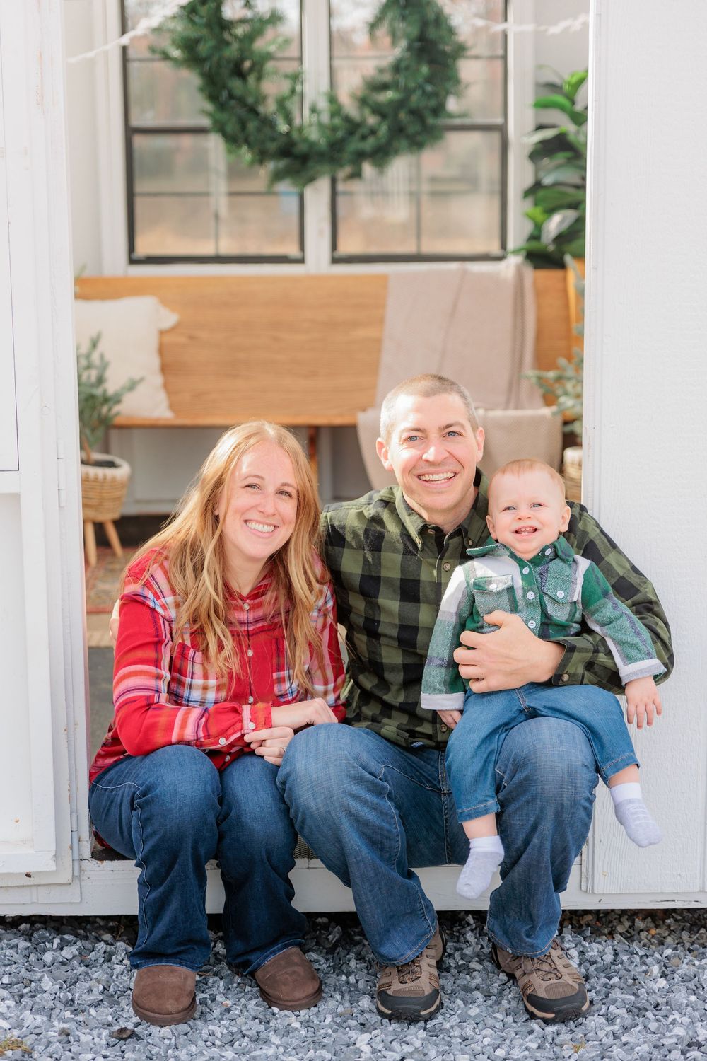 A group in festive plaid and denim sit together on a white porch with garland and Christmas wreaths in the background at Turkey Trac Farm