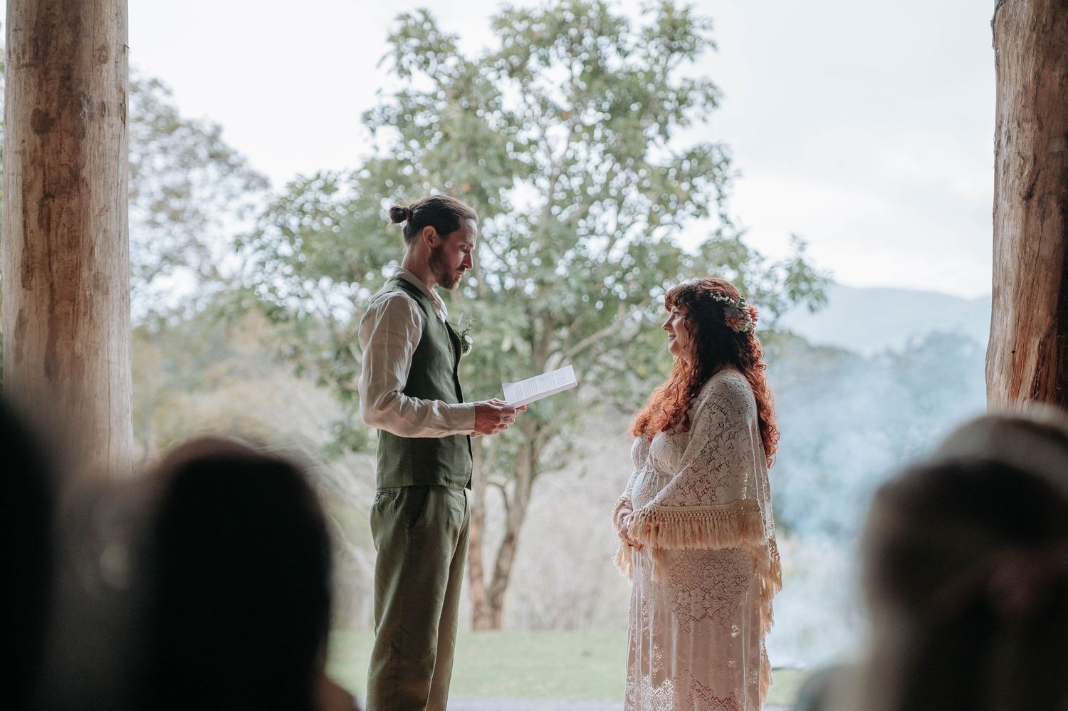 A panoramic view of an outdoor rustic wedding ceremony under wooden posts with mountains in the distance.