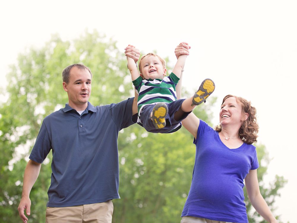 Parents swinging child at park; outdoor family portrait session in Ann Arbor, Michigan.