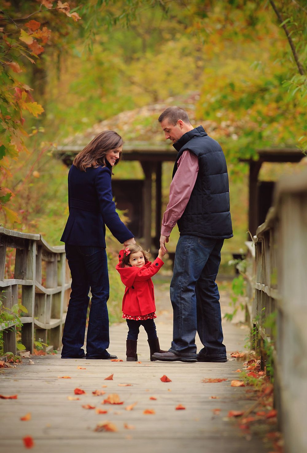 Family autumn portrait session by Brighton photographer in Ann Arbor, MI ; Family, parents and toddler on bridge at park with fall colors