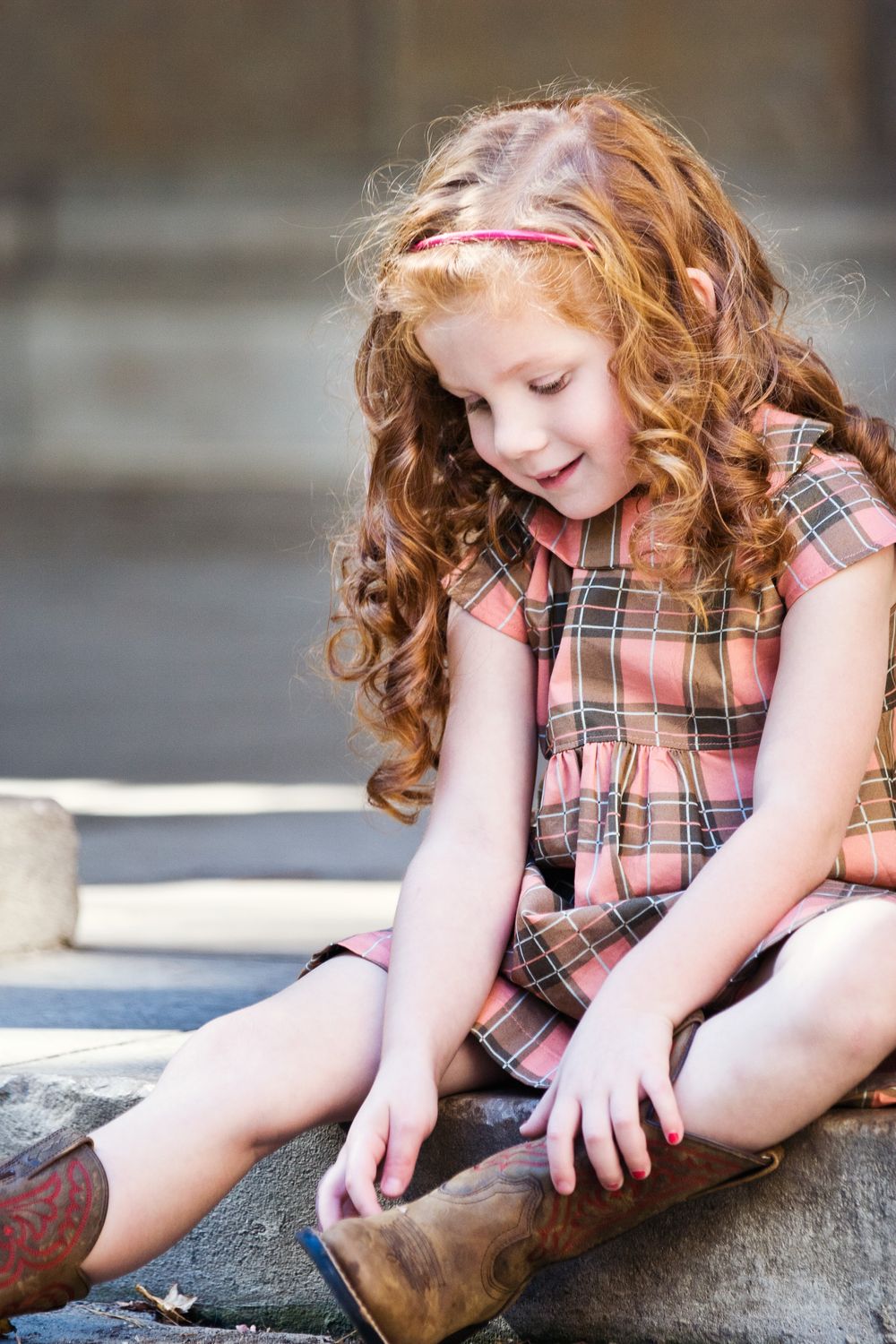 Girl smiling and playing with her boots; family and child portrait photography session in Ann Arbor, Michigan.